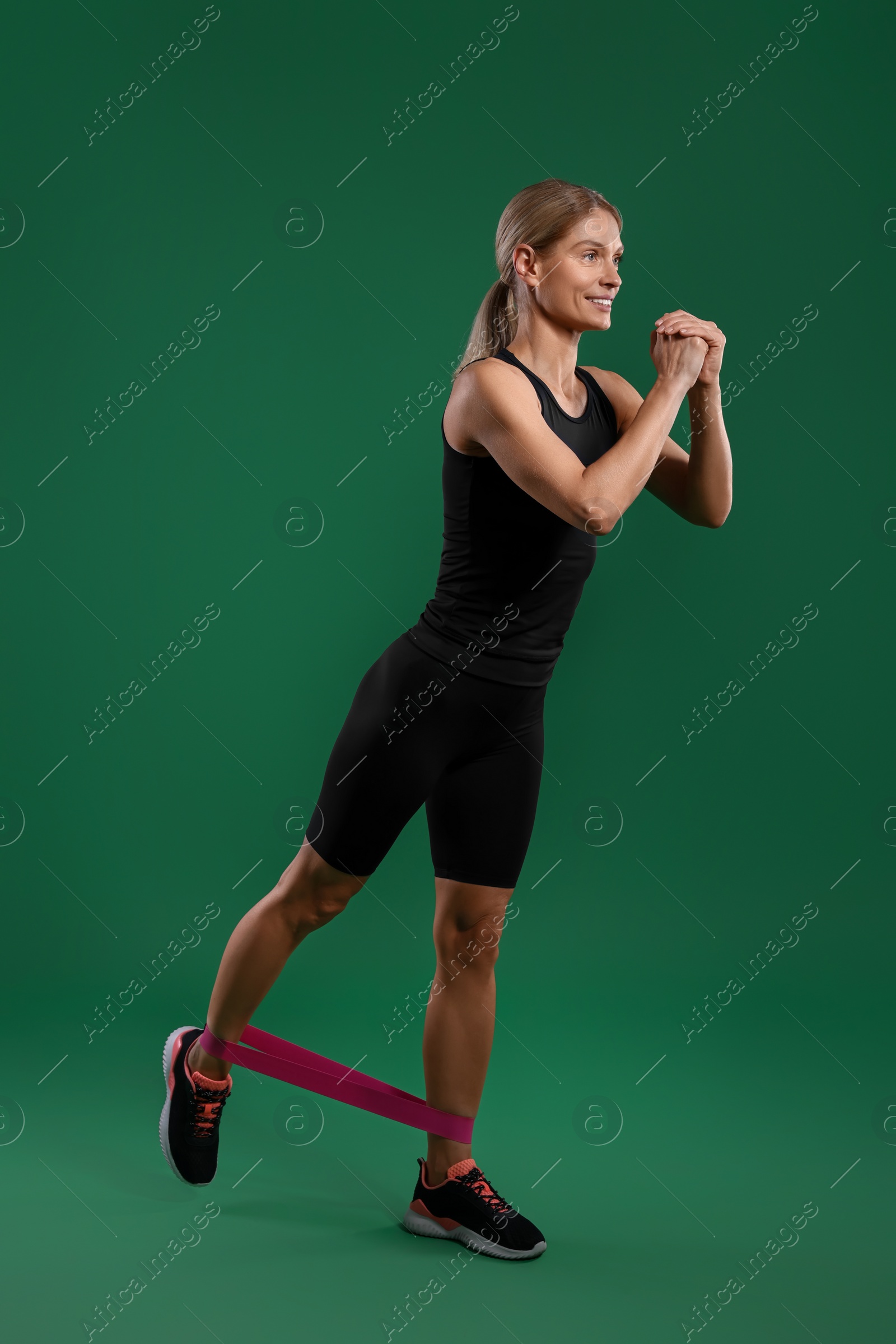 Photo of Smiling woman exercising with elastic resistance band on green background