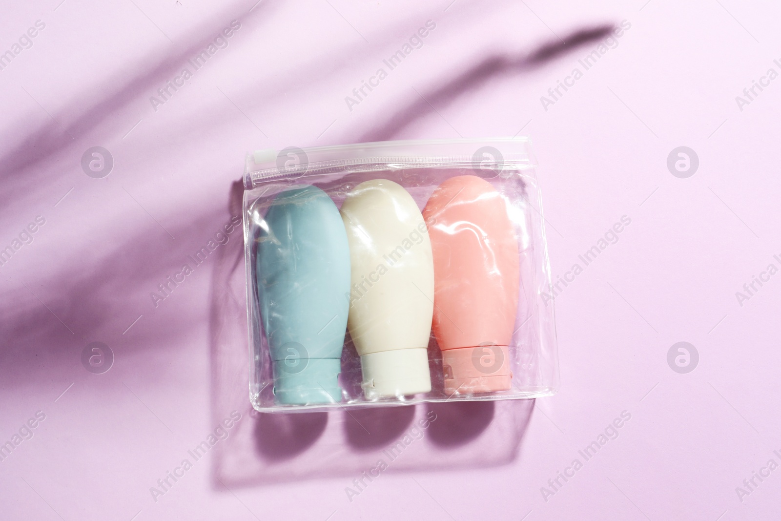 Photo of Cosmetic travel kit in plastic bag on violet background, top view