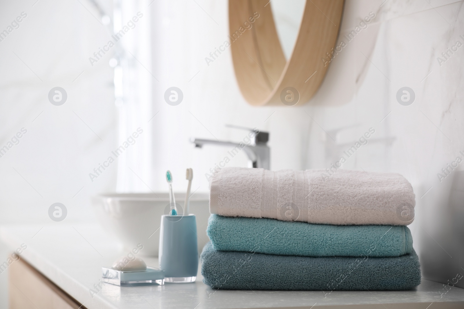 Photo of Stack of fresh towels, toothbrushes and soap bar on countertop in bathroom