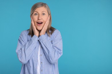 Portrait of surprised senior woman on light blue background, space for text