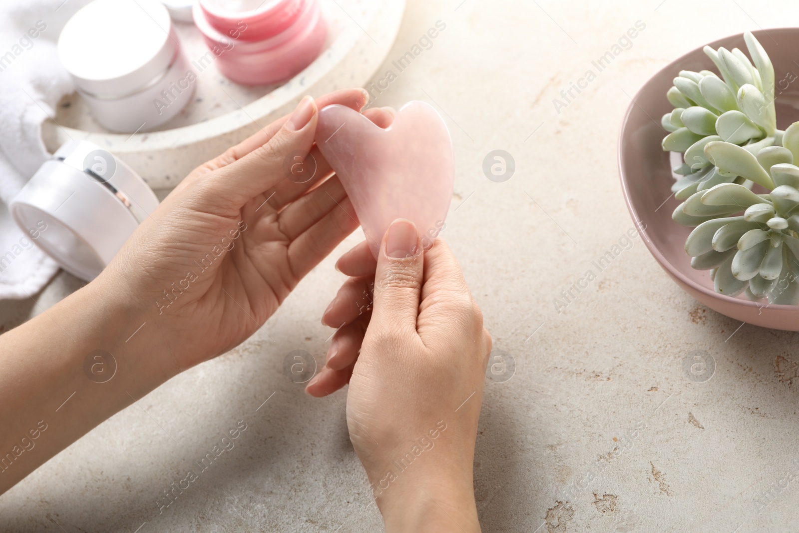 Photo of Woman holding gua sha tool over light stone table, closeup