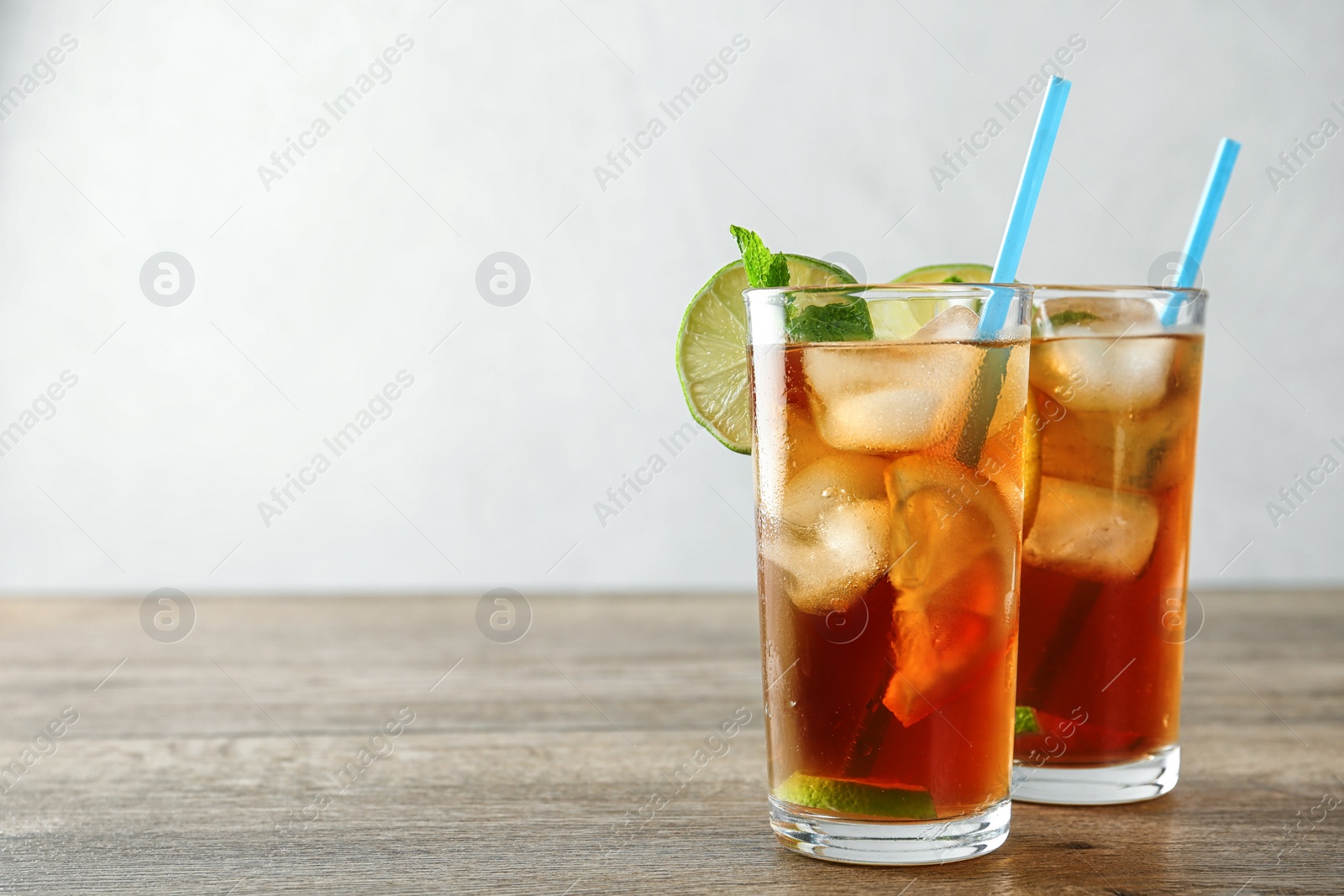 Photo of Glasses of refreshing iced tea on wooden table against light background. Space for text