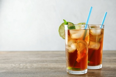 Glasses of refreshing iced tea on wooden table against light background. Space for text