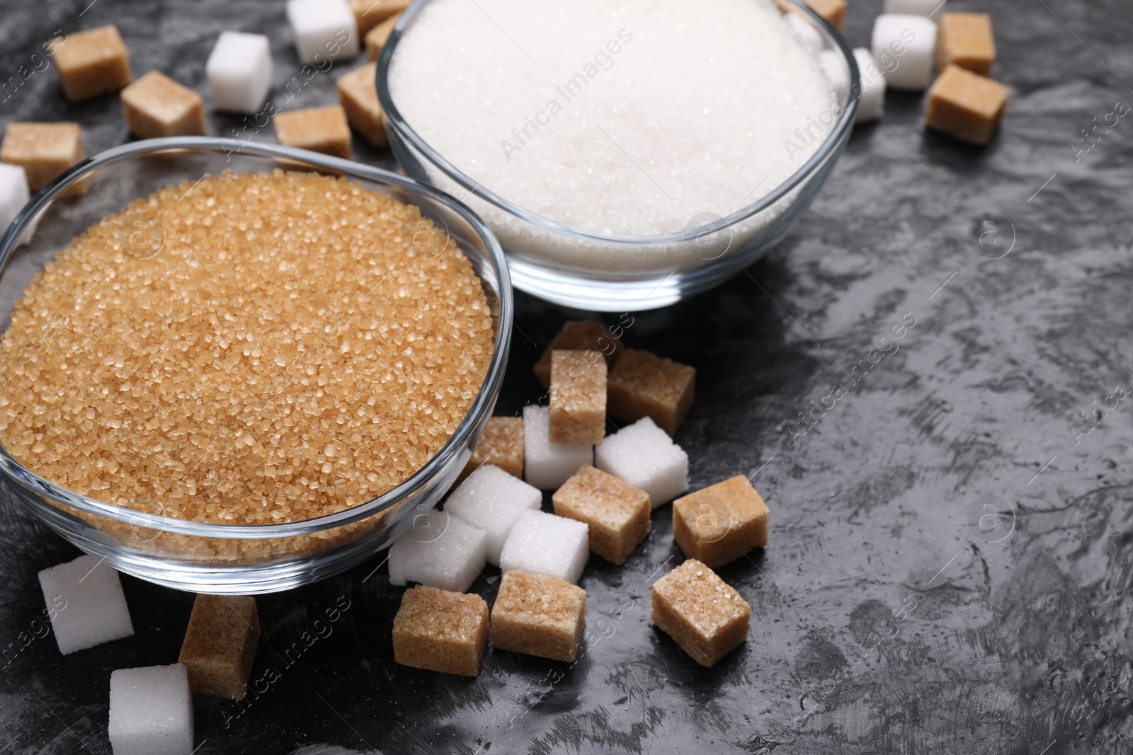 Photo of Different types of sugar in bowls on dark gray textured table, closeup. Space for text