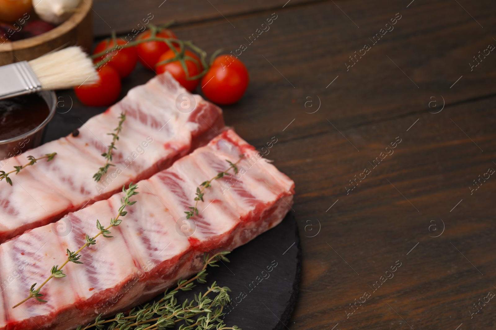 Photo of Fresh raw pork ribs with thyme on wooden table, closeup. Space for text