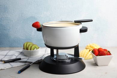 Photo of White chocolate fondue in pot and fresh fruits on gray table