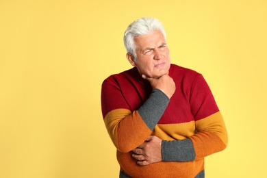 Senior man suffering from sore throat on yellow background. Cold symptoms