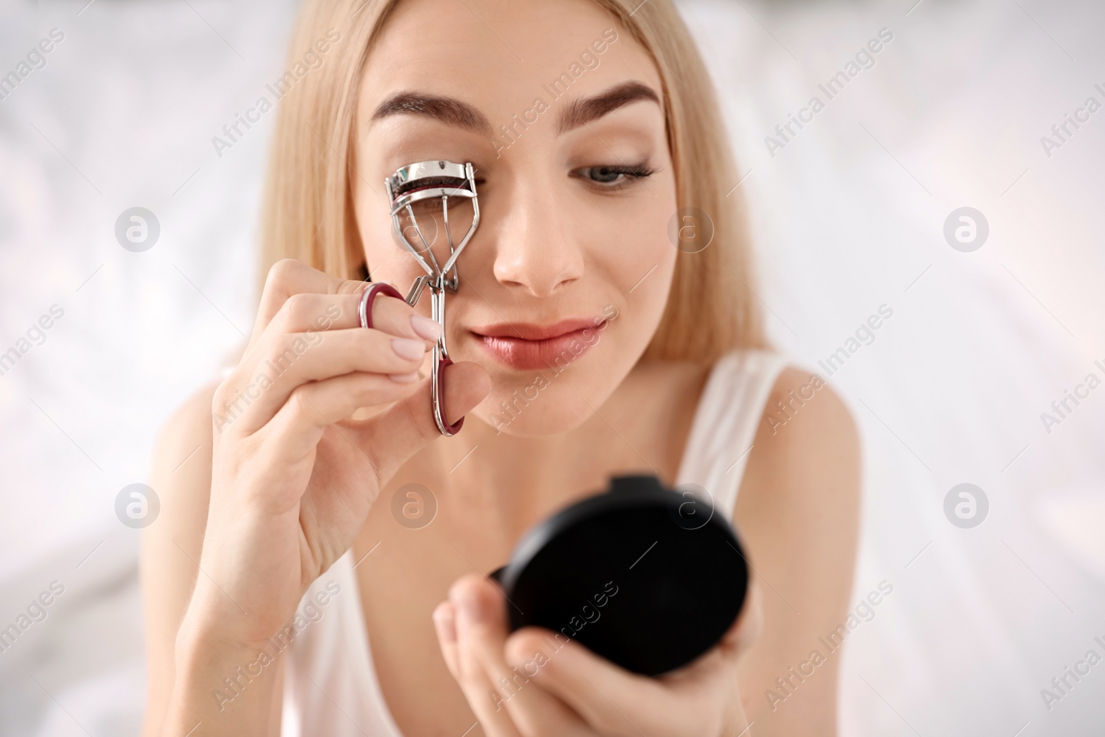 Photo of Young woman curling her eyelashes at home