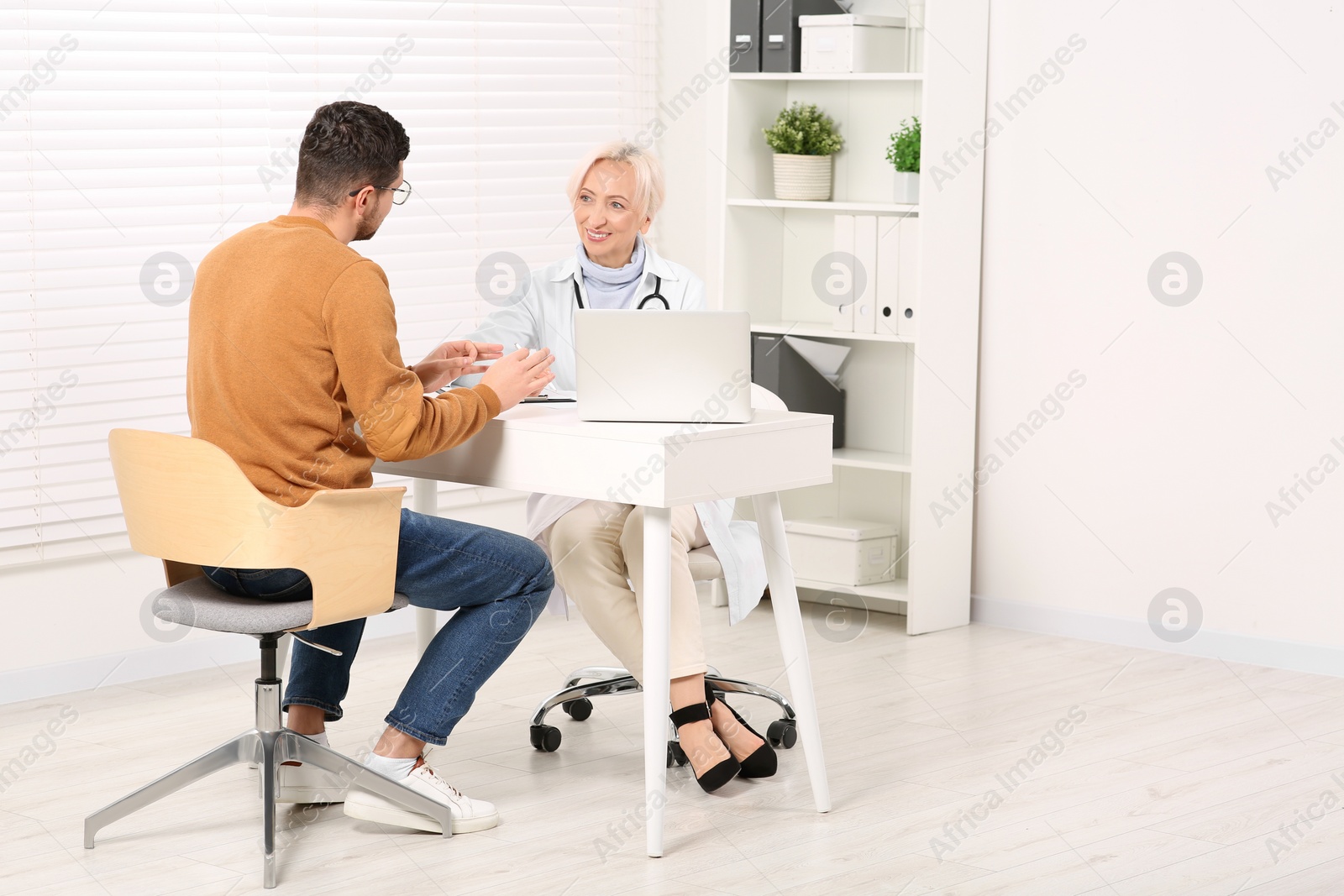 Photo of Doctor consulting patient at white table in clinic