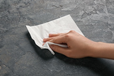 Woman wiping grey table with paper napkin, closeup