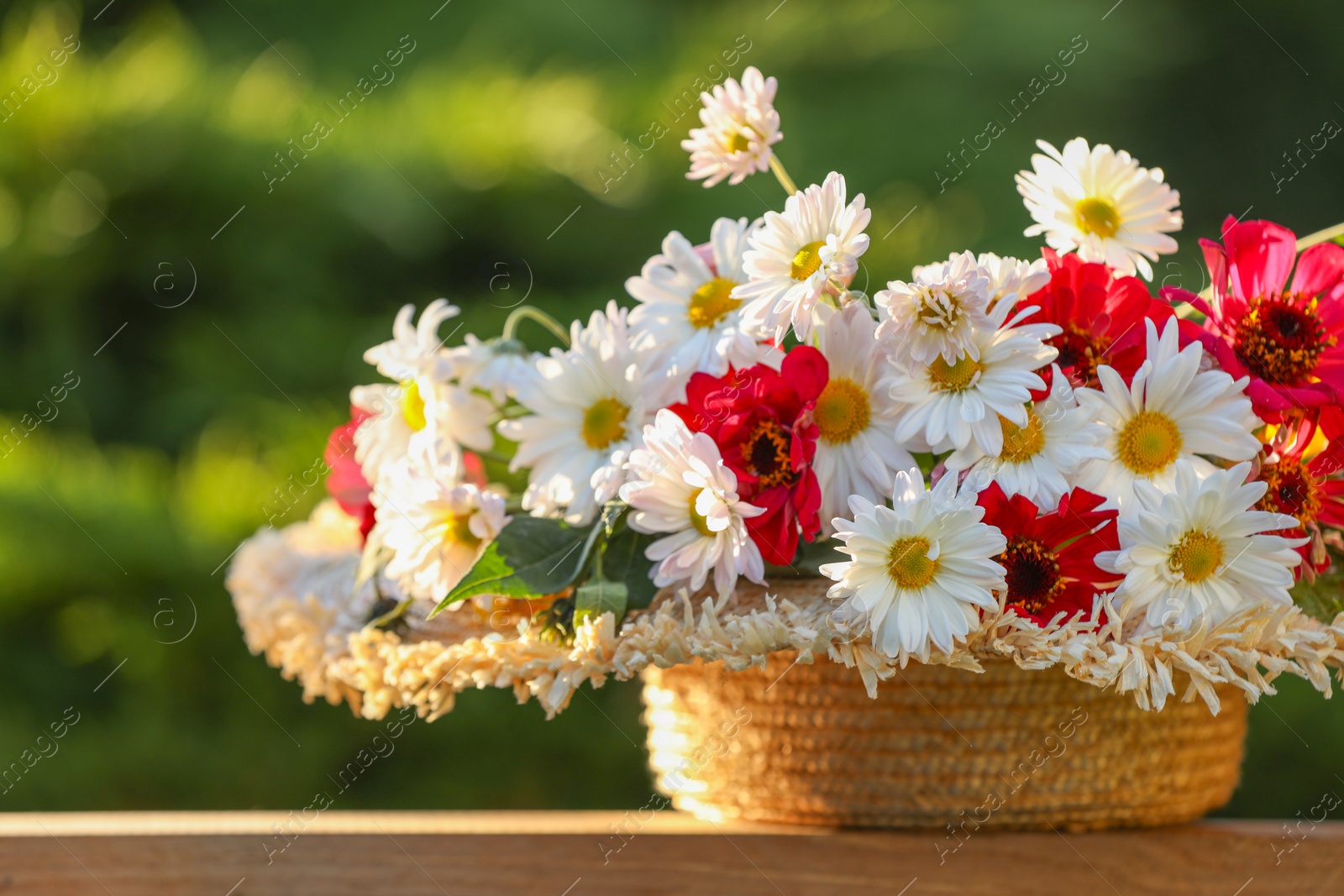 Photo of Beautiful wild flowers in wicker basket on wooden table against blurred background