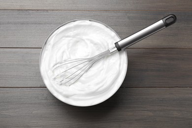 Photo of White cream with balloon whisk on grey wooden table, top view