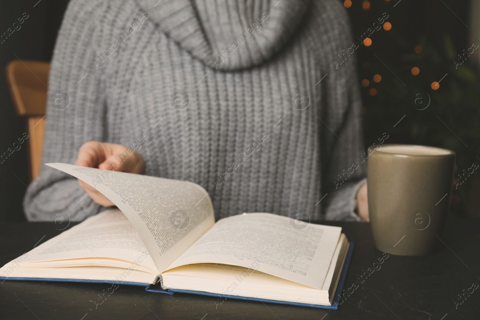 Image of Woman with cup of coffee reading book at table, closeup