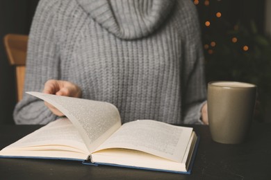 Woman with cup of coffee reading book at table, closeup