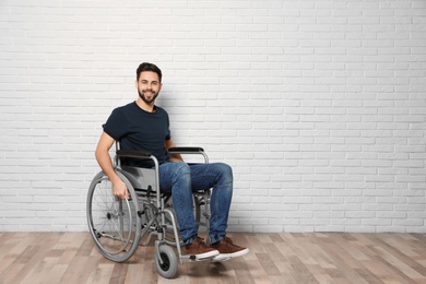 Photo of Young man in wheelchair near brick wall indoors. Space for text