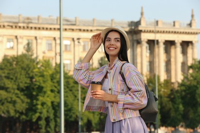 Beautiful young woman with stylish backpack and coffee on city street, space for text