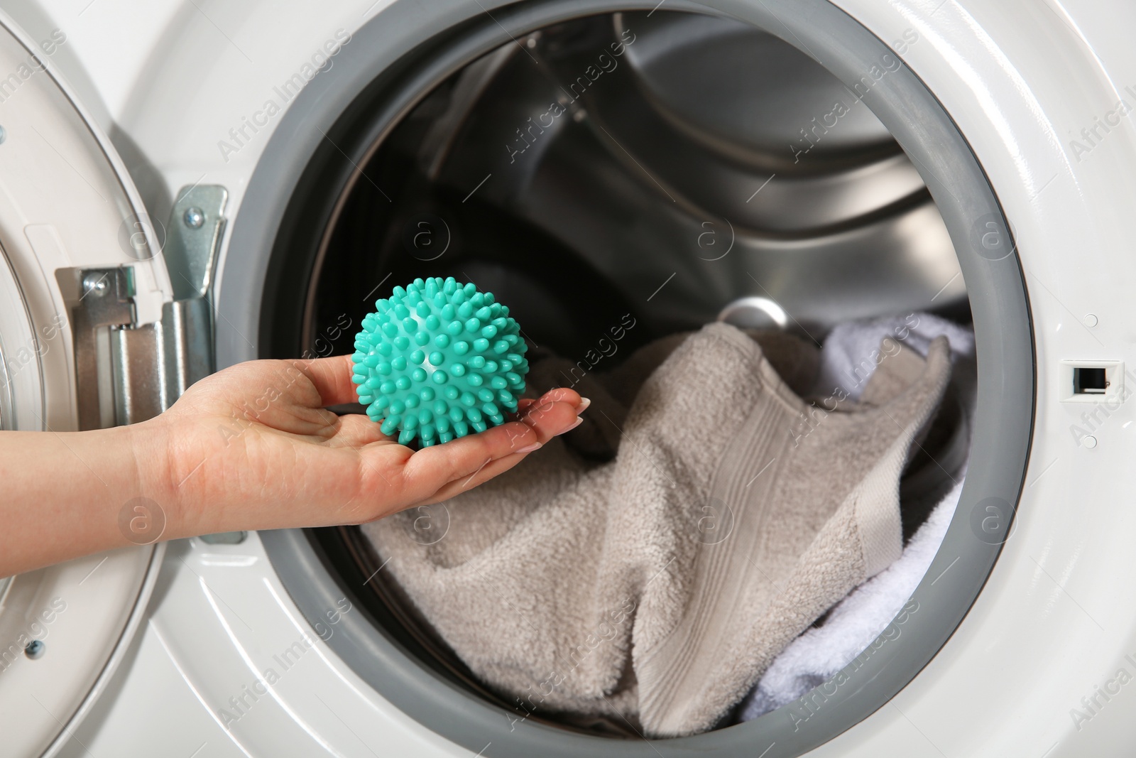 Photo of Woman putting green dryer ball into washing machine, closeup