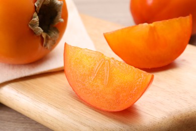 Photo of Delicious ripe persimmons on wooden board, closeup
