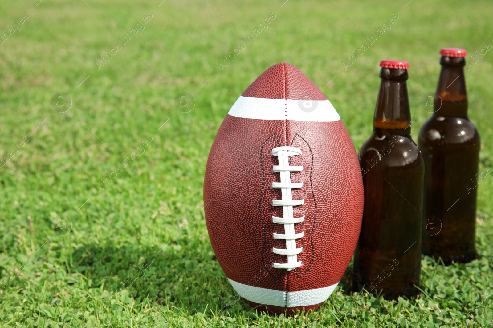 Photo of Ball for American football and beverage on fresh green field grass. Space for text