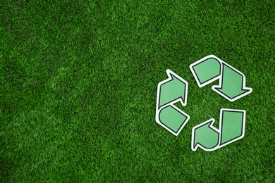 Photo of Paper recycling symbol on green grass, top view. Space for text