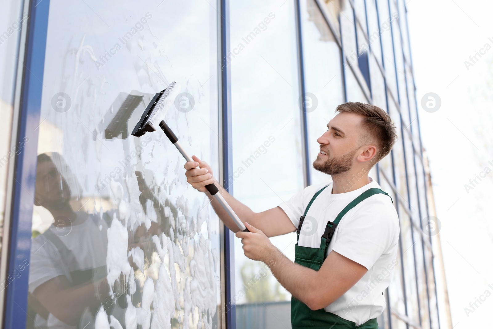 Photo of Male cleaner wiping window glass with squeegee from outside