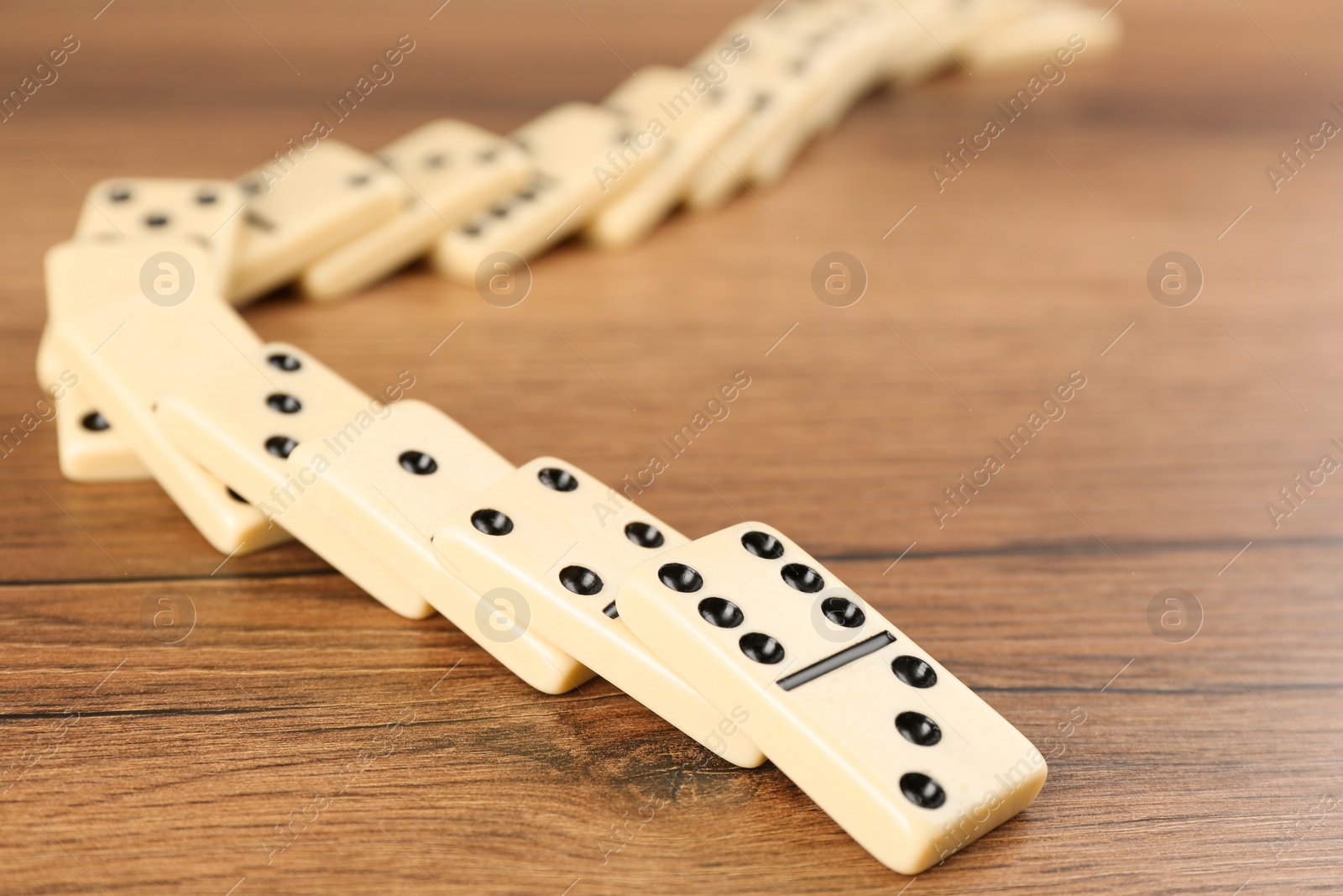 Photo of Fallen white domino tiles on wooden table