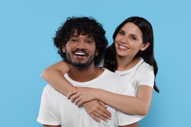 International dating. Happy couple hugging on light blue background