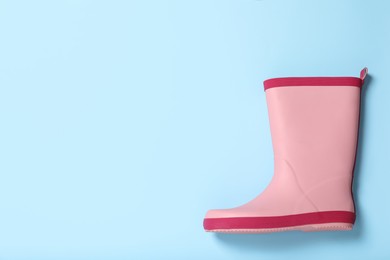 Pink rubber boot on light blue background, top view. Space for text