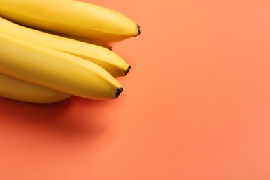 Photo of Ripe yellow bananas on coral background, closeup. Space for text