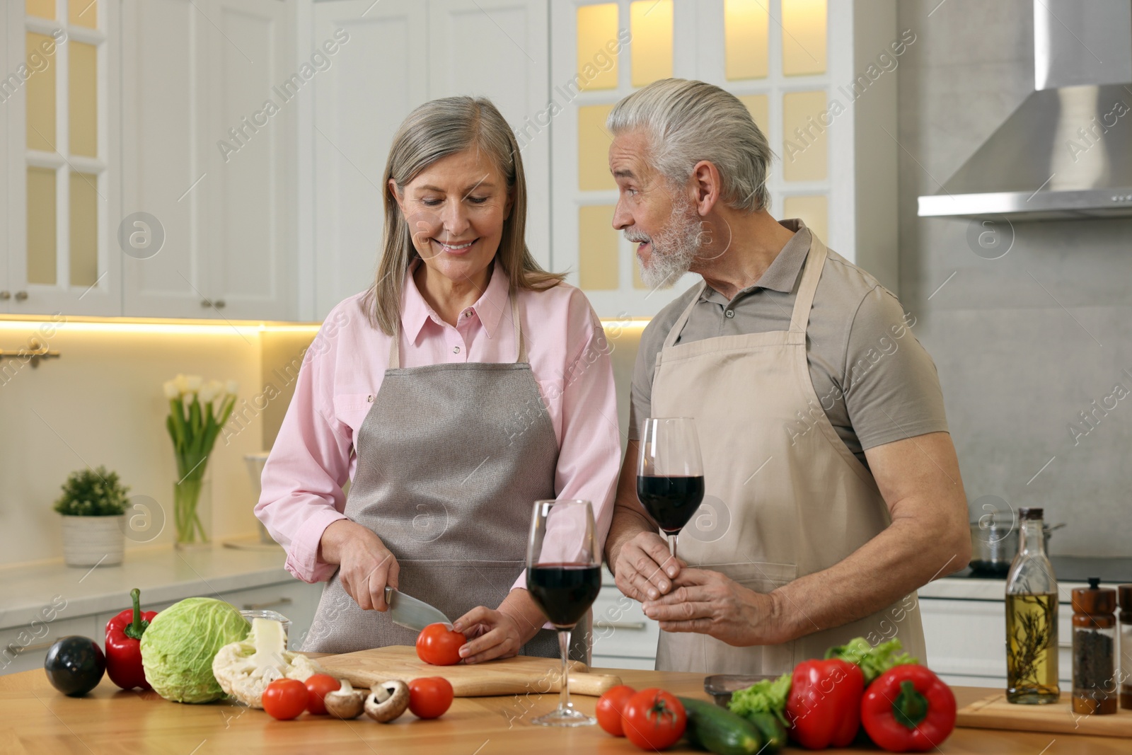 Photo of Happy senior couple cooking together in kitchen. Man with glass of wine near his wife