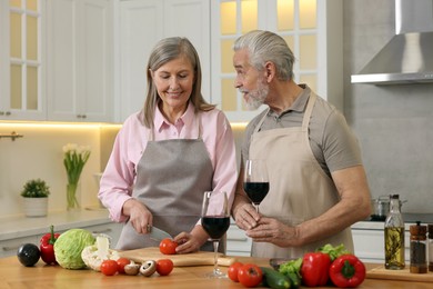 Happy senior couple cooking together in kitchen. Man with glass of wine near his wife