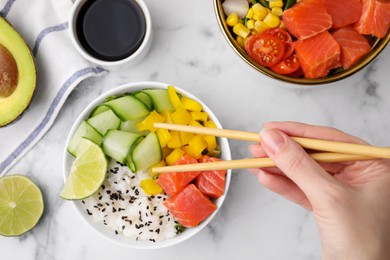 Woman eating delicious poke bowl with salmon, lime and vegetables on white marble table, top view