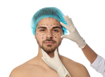 Doctor examining man's face with marker lines for plastic surgery operation on white background