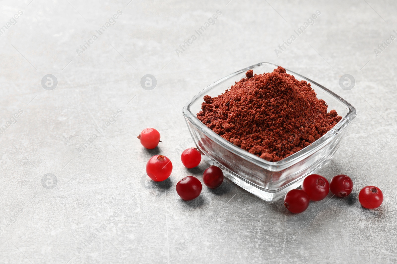 Photo of Cranberry powder in bowl and fresh berries on light grey table. Space for text