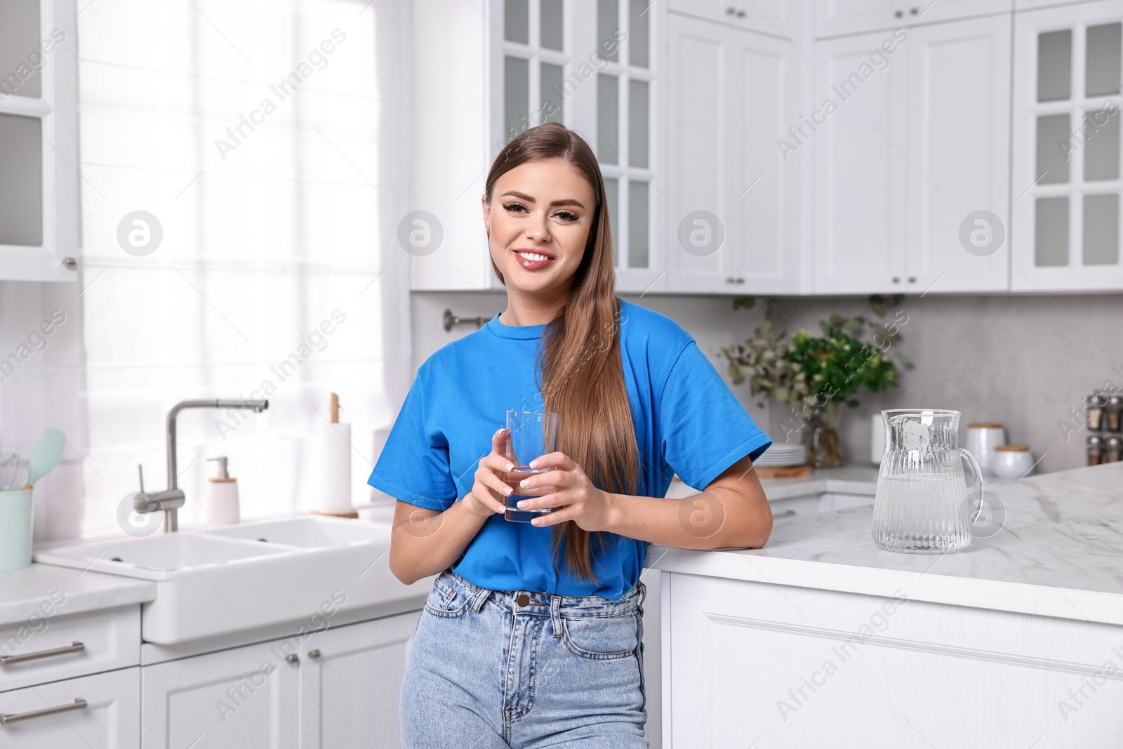 Photo of Happy woman with glass of fresh water in kitchen