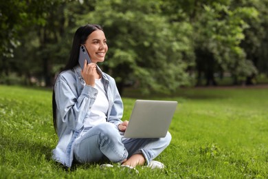 Photo of Happy young woman using modern laptop and talking on phone in park. Space for text