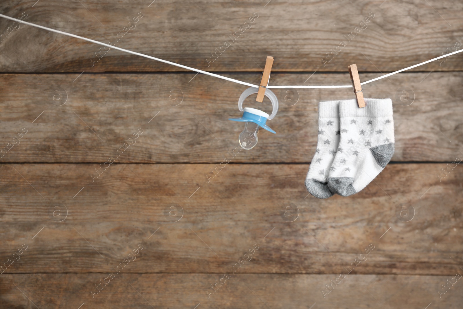 Photo of Pair of socks and pacifier on laundry line against wooden background, space for text. Baby accessories