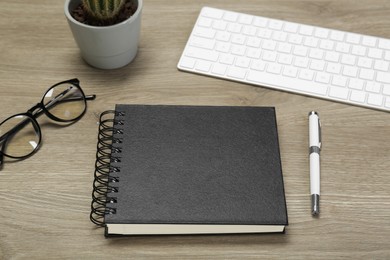 Photo of Black notebook, keyboard and pen on wooden table