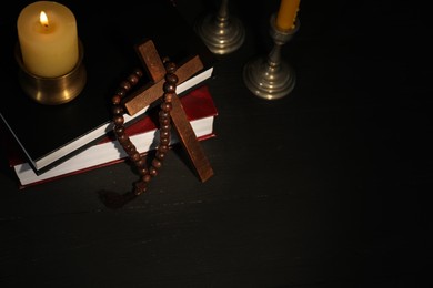 Church candles, Bible, rosary beads and cross on black wooden table, above view. Space for text