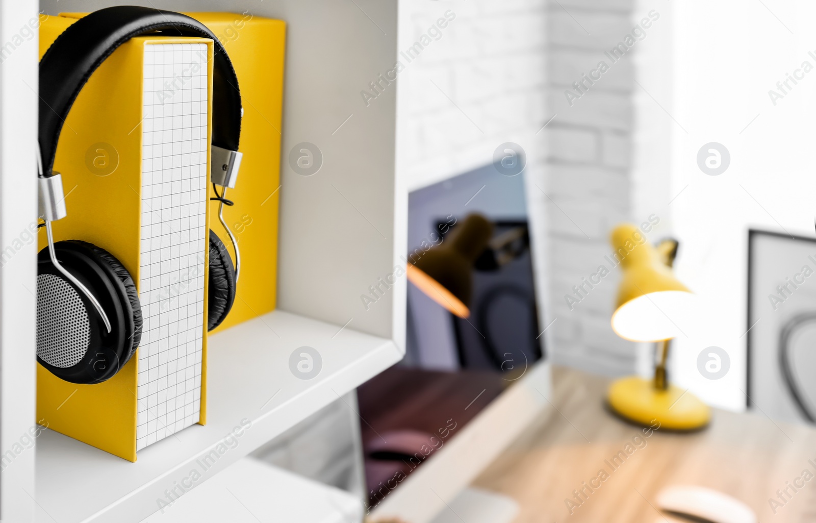 Photo of Workplace with folder and headphones on shelf over desk at home