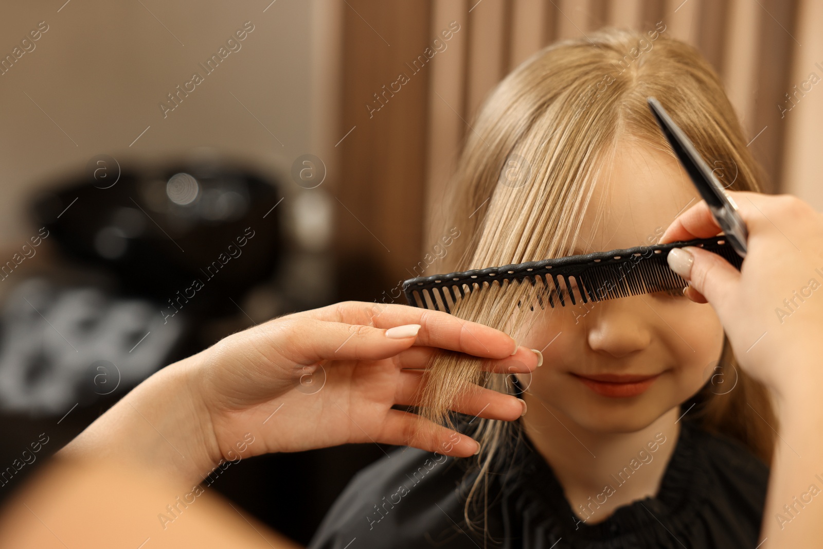 Photo of Professional hairdresser combing girl's hair in beauty salon, closeup