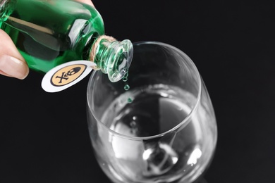 Photo of Woman pouring poison into glass of water on black background, closeup