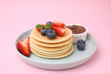 Delicious pancakes with strawberries, blueberries and chocolate sauce on pink background