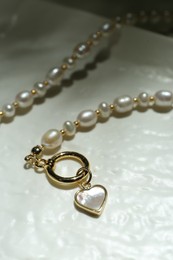 Elegant pearl necklace on white textured surface, closeup