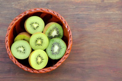 Photo of Bowl of many cut fresh kiwis on wooden table, top view. Space for text