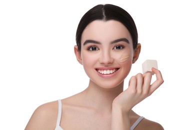 Teenage girl applying foundation on face with makeup sponge against white background