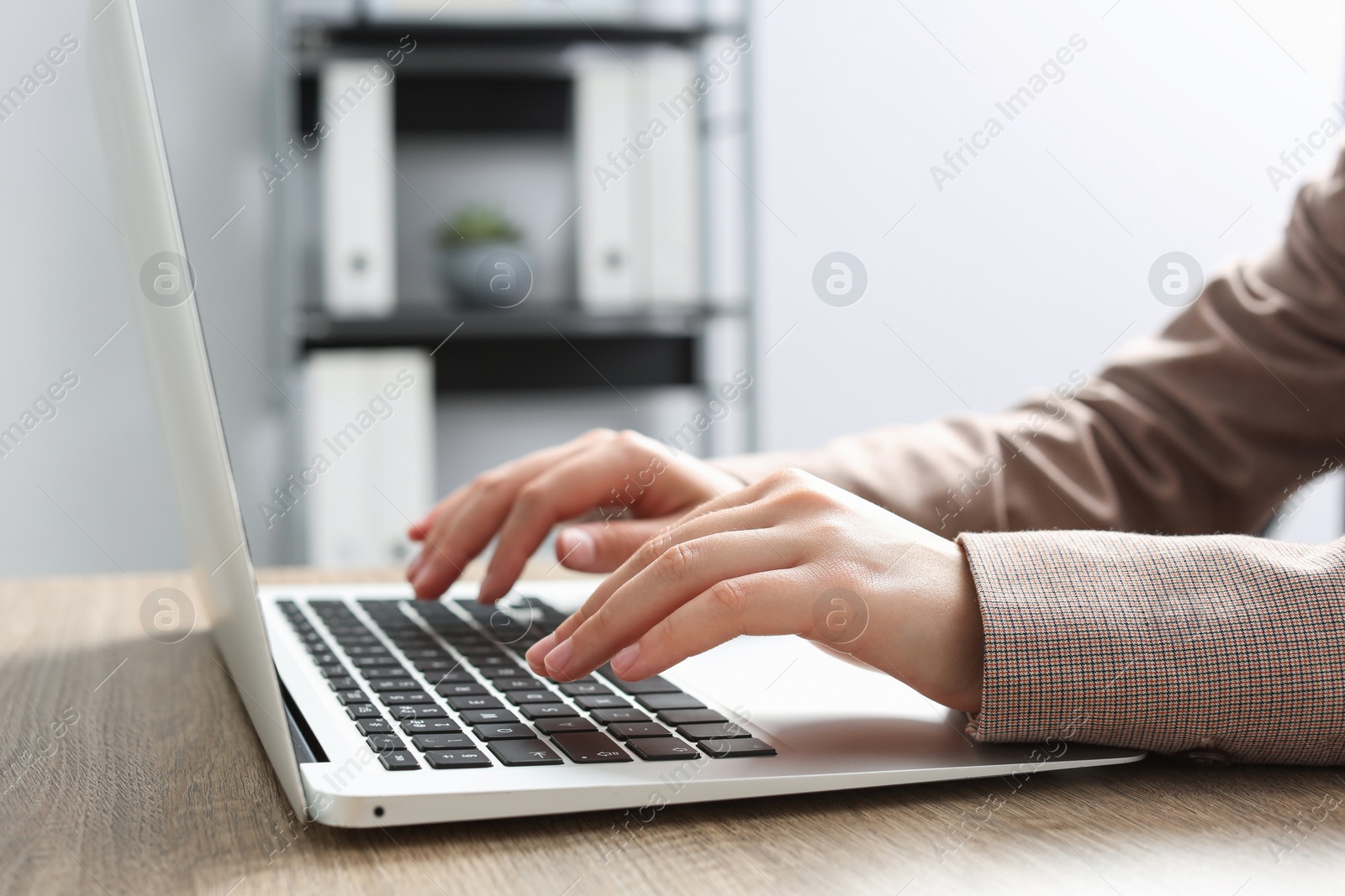 Photo of Woman working on laptop at wooden table in office, closeup