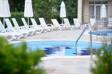 Outdoor swimming pool with handrails and many empty sunbeds at resort on sunny day