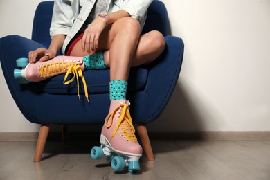 Photo of Young woman with retro roller skates in armchair against light wall, closeup. Space for text