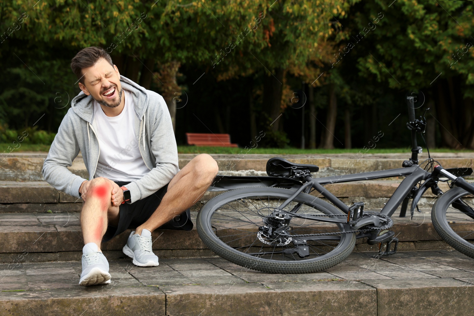 Image of Man with injured knee on steps near bicycle outdoors